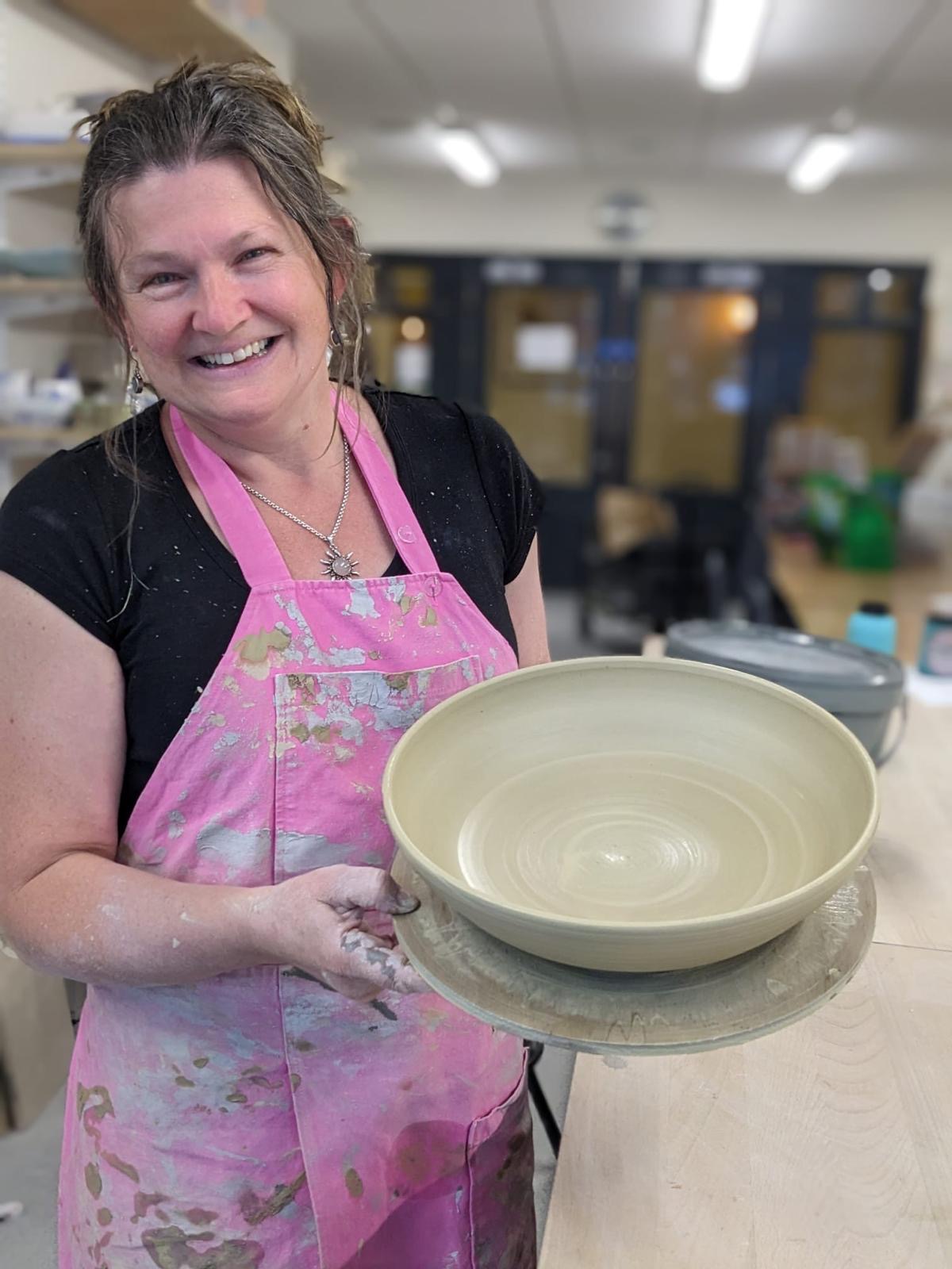 Ellie in her studio holding a freshly thrown stoneware bowl, hands clay-stained, smiling