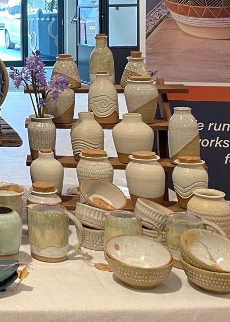 Speckled cream vases and bottles with carved wave patterns on a tiered wooden stand, with a jar of bluebells