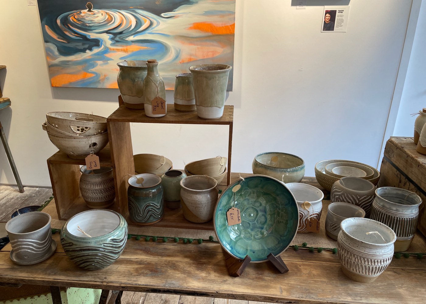 A long table of Ellie's carved planters, bowls and jugs beneath a large painting in a gallery space