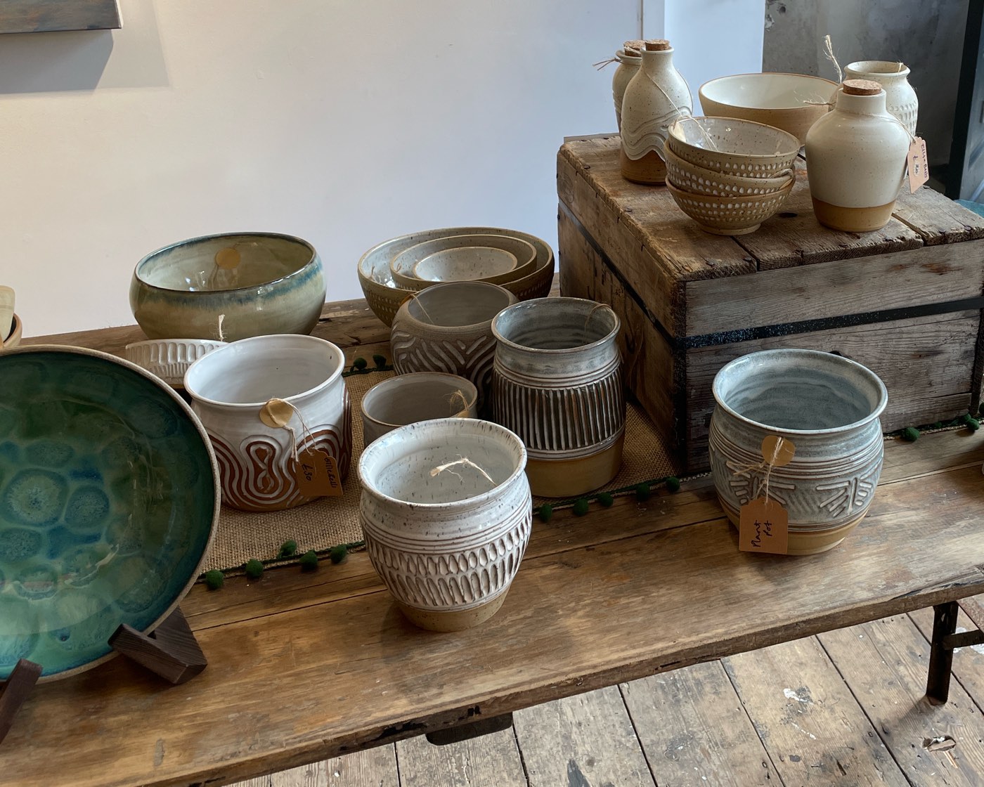 Carved stoneware planters and bowls on a burlap runner, with corked bottles on a wooden crate