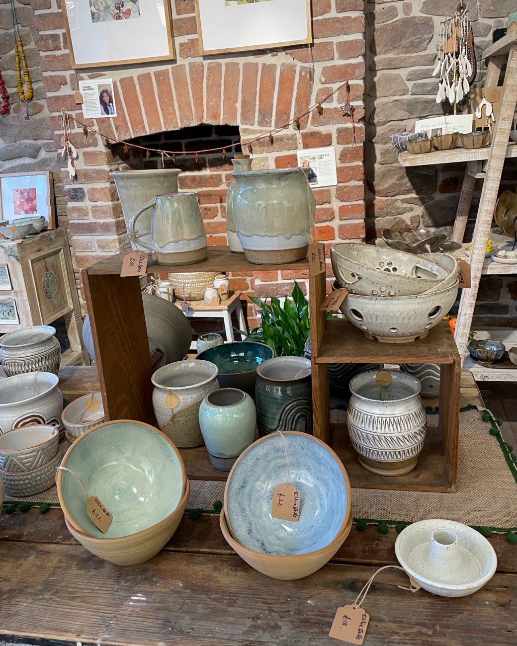 Drip-glazed jugs, jars and berry bowls on old wooden crates in front of a brick fireplace
