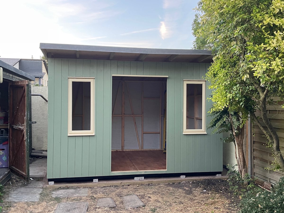The sage-green studio shell standing, with two windows and an open doorway