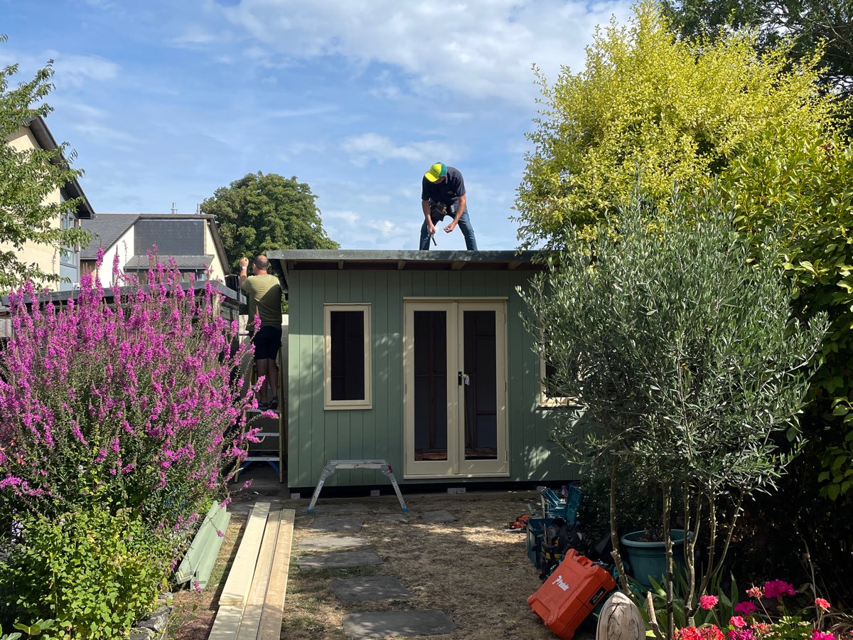 A builder working on the roof of the green studio, with the double doors fitted