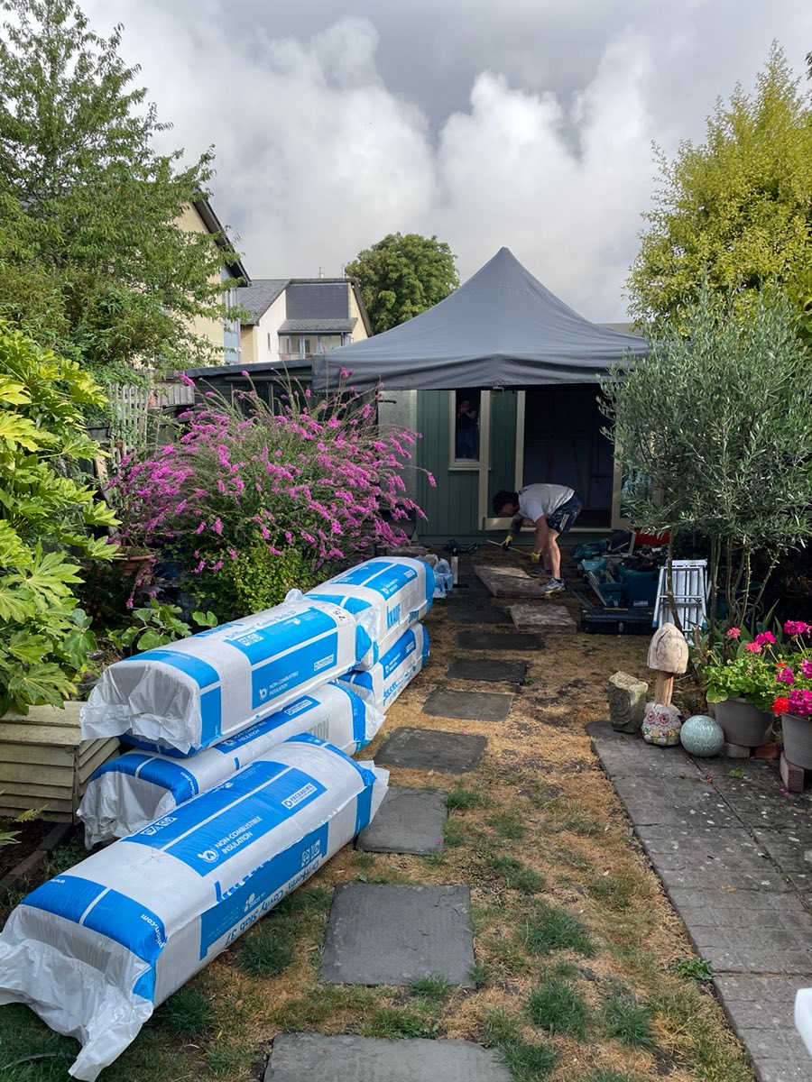 Rolls of insulation stacked on the garden path, with the studio under a gazebo behind