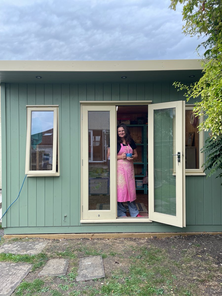 Ellie standing in the doorway of the sage-green studio, seen from the lawn