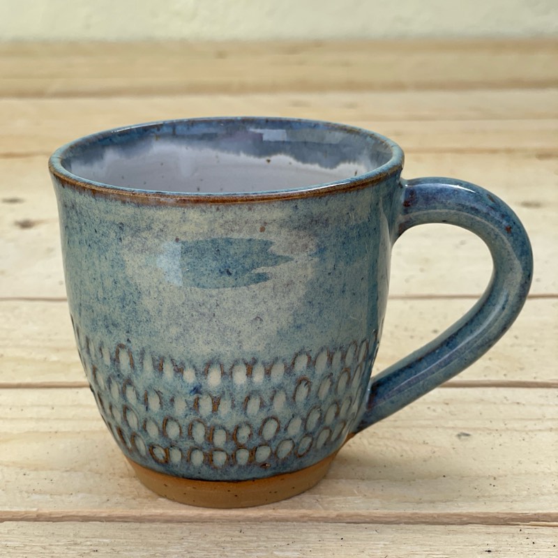 Speckled blue mug with a band of carved dots above a bare clay foot