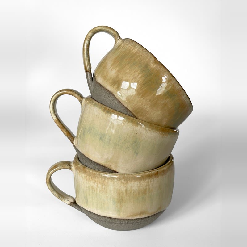 Three iron lustre cappuccino cups stacked, glaze shading from honey to soft green