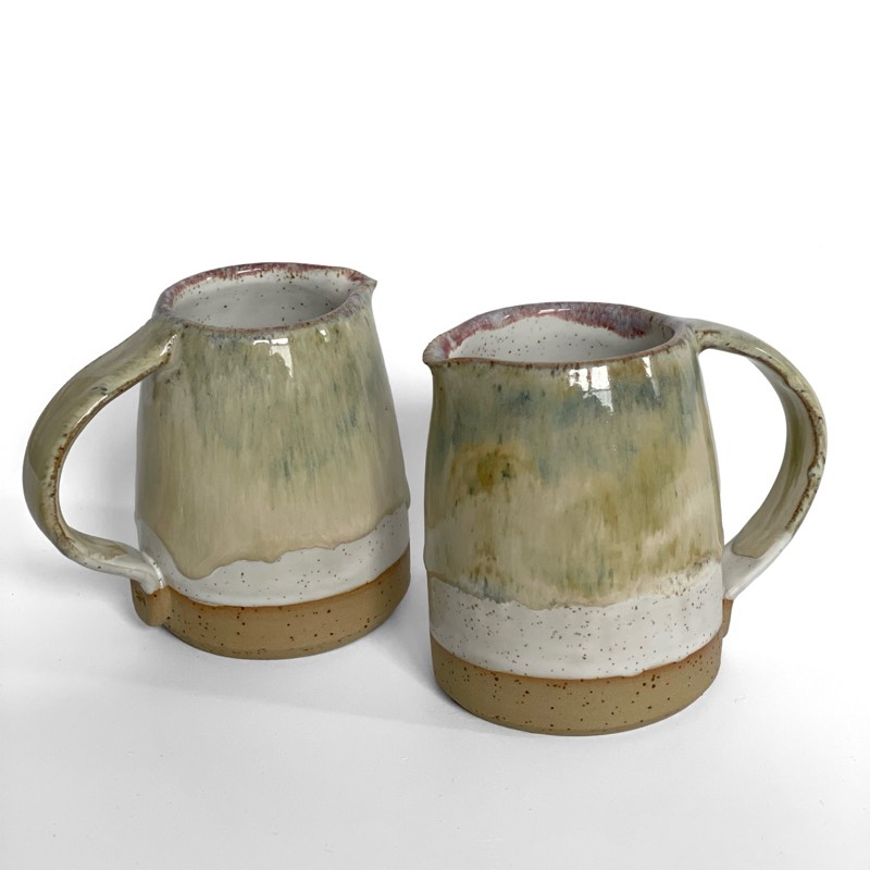 Two iron lustre mugs with pale green drips over a white base