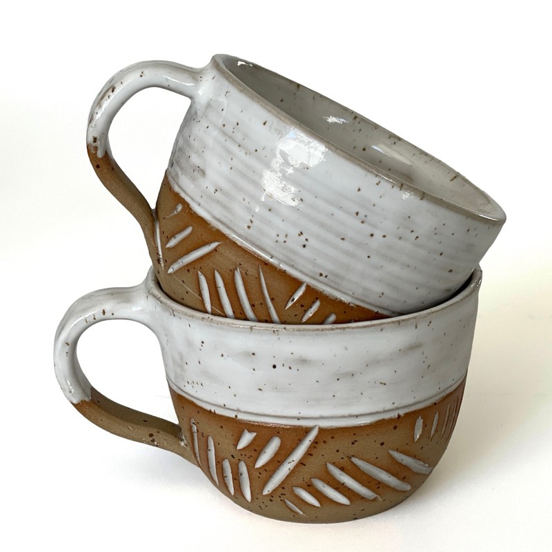 Two white and speckled clay mugs carved with dashes, stacked