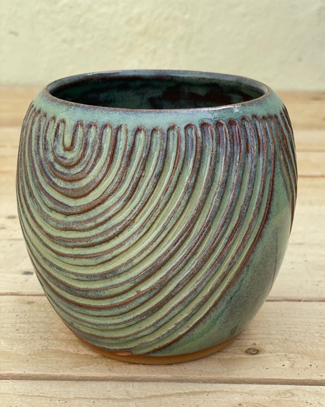 Teal and green vessel carved with concentric arches, on a wooden table