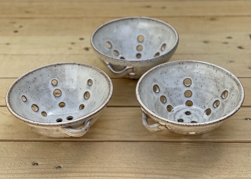 Three white speckled berry bowls on a wooden table